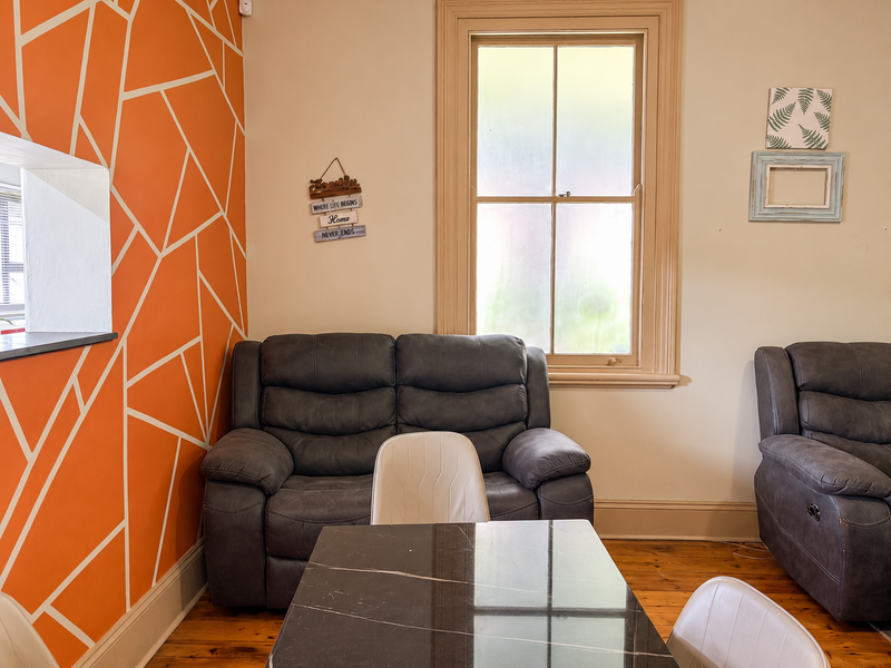 A living area featuring original timber flooring, a classic sash window with timber framing, and a decorative accent wall.