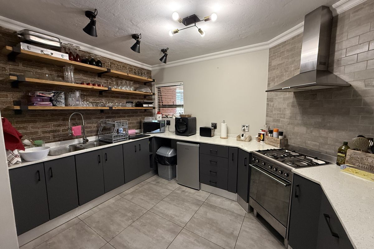 Modern kitchen featuring dark cabinetry, stone countertops, exposed brick wall with open shelving, and high-quality stainless steel appliances including a gas hob and extractor.