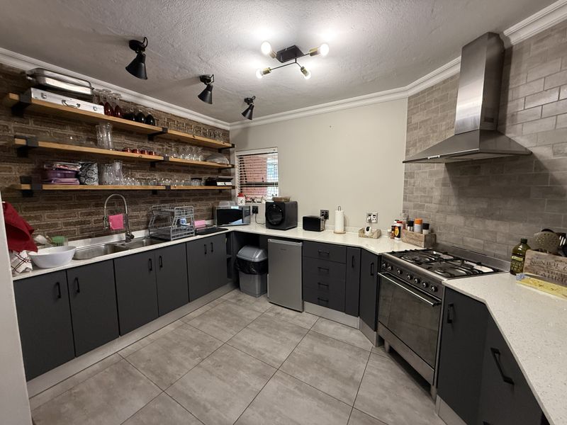 Modern kitchen featuring dark cabinetry, stone countertops, exposed brick wall with open shelving, and high-quality stainless steel appliances including a gas hob and extractor.