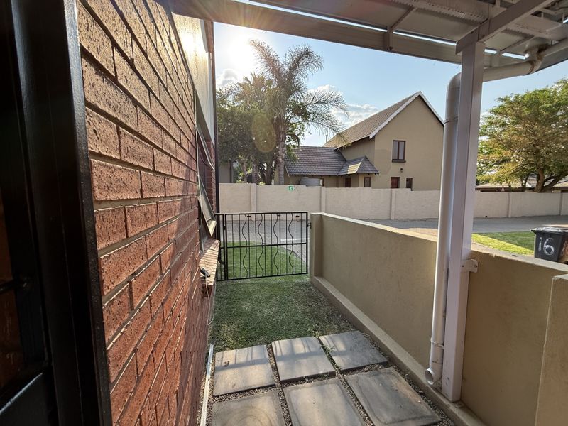 A covered patio area featuring brick wall construction, paved flooring, and a metal gate leading to the garden space.