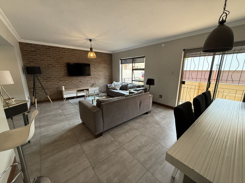 Spacious open-plan living and dining area featuring modern tiled flooring, an exposed brick feature wall, and direct access to an outdoor space.