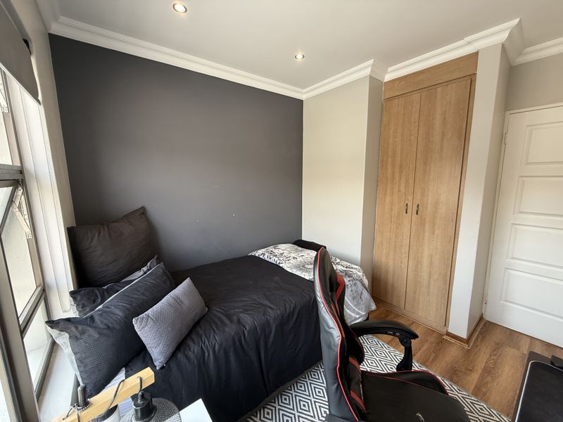 A well-maintained bedroom featuring laminate flooring, recessed downlighting, and a built-in wooden wardrobe with a modern dark accent wall.