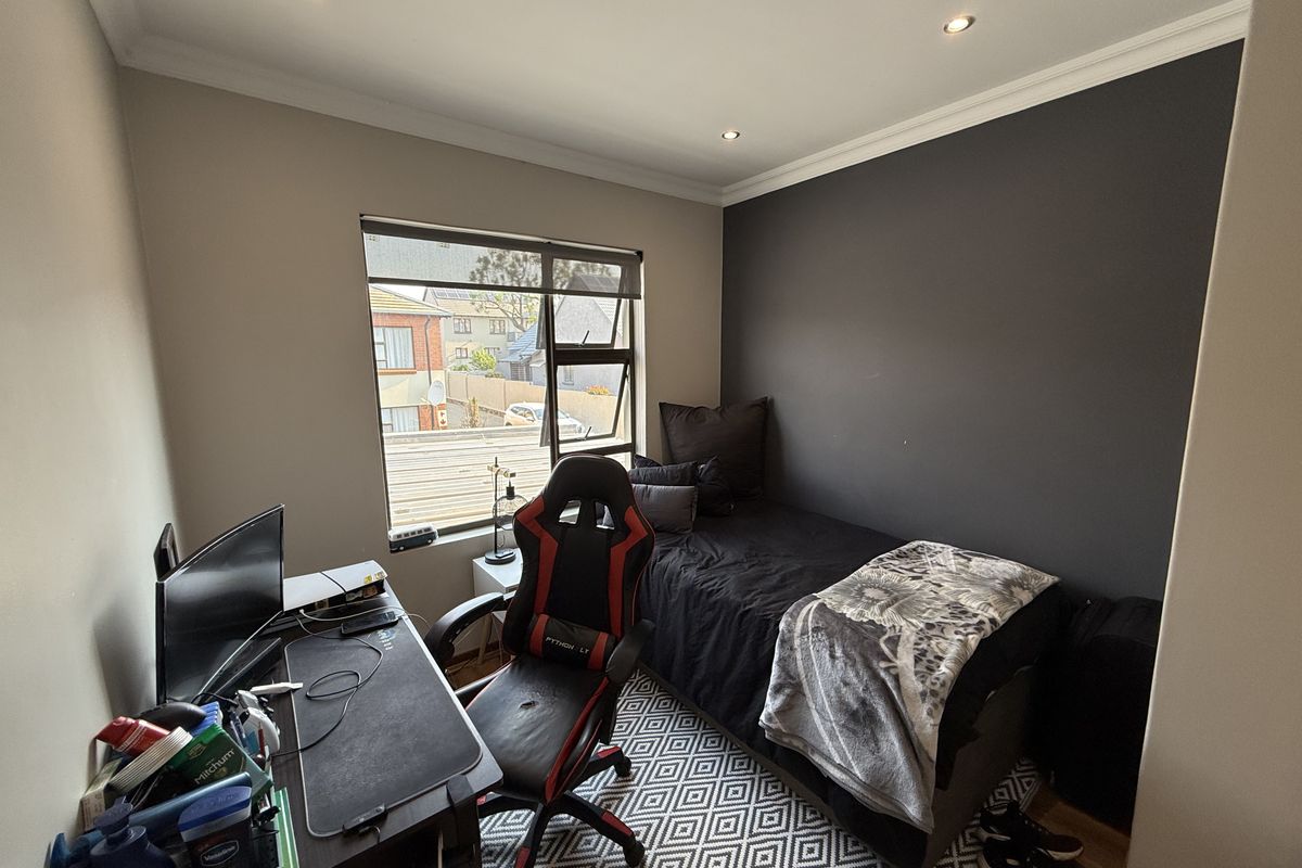 A compact bedroom featuring a dark accent wall, recessed downlighting, and an aluminium-framed window providing natural light.