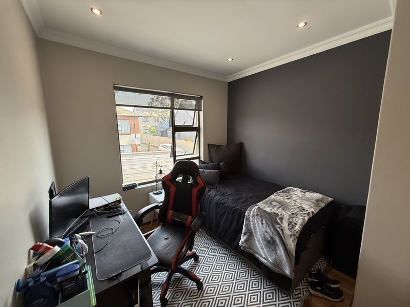 A compact bedroom featuring a dark accent wall, recessed downlighting, and an aluminium-framed window providing natural light.