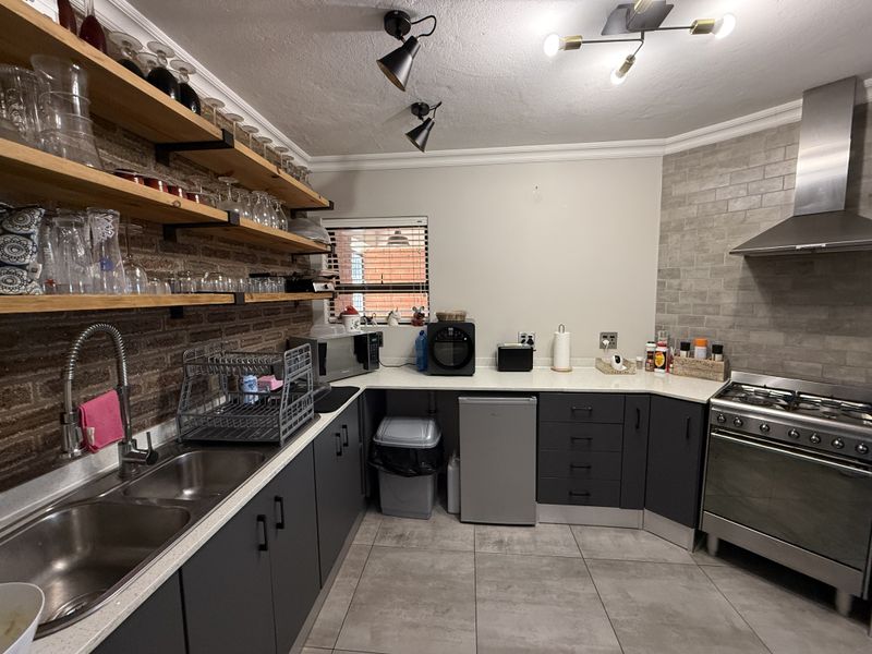 Modern kitchen featuring dark cabinetry, exposed brick wall with timber shelving, stainless steel gas stove, and grey subway tile splashback.