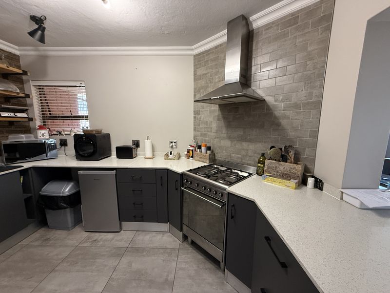 Modern kitchen featuring dark cabinetry, quartz countertops, a gas hob with stainless steel extractor fan, and a stylish tiled backsplash.