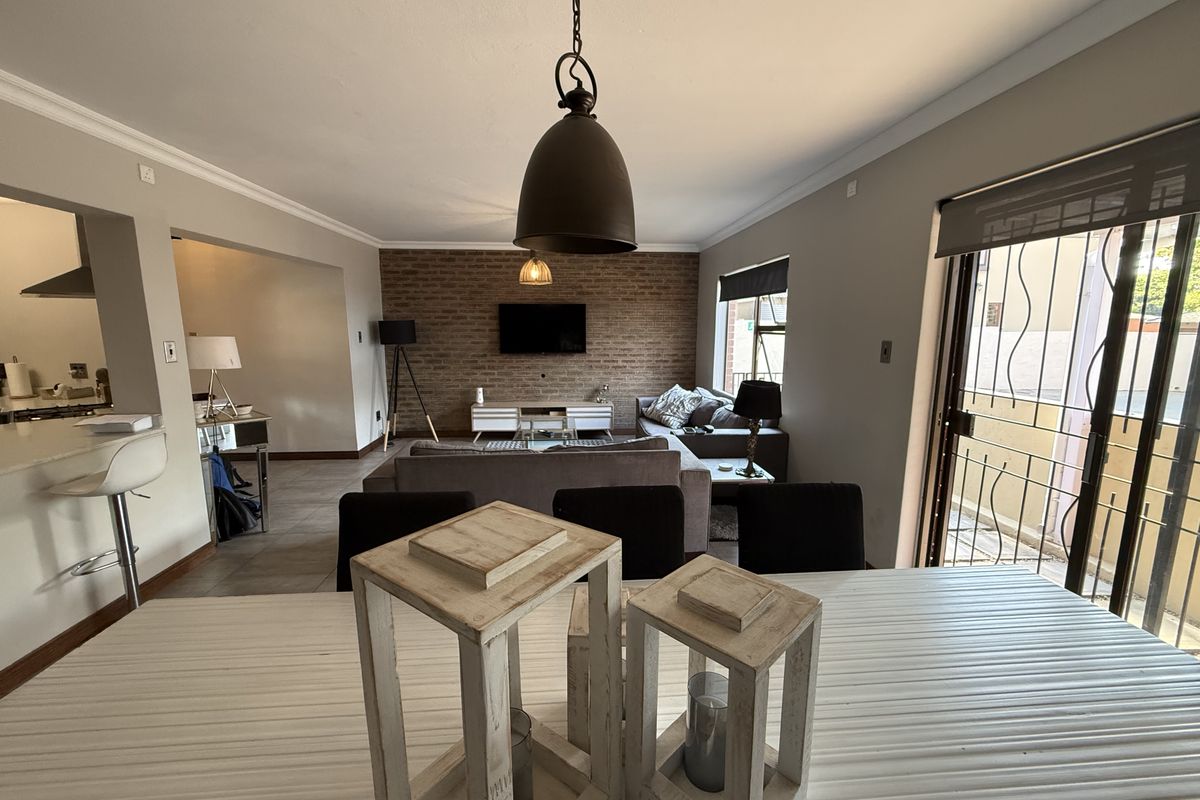 Spacious open-plan living and dining area featuring an exposed brick feature wall, tiled flooring, and direct access to an outdoor patio through sliding doors.