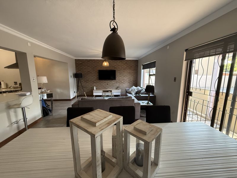 Spacious open-plan living and dining area featuring an exposed brick feature wall, tiled flooring, and direct access to an outdoor patio through sliding doors.