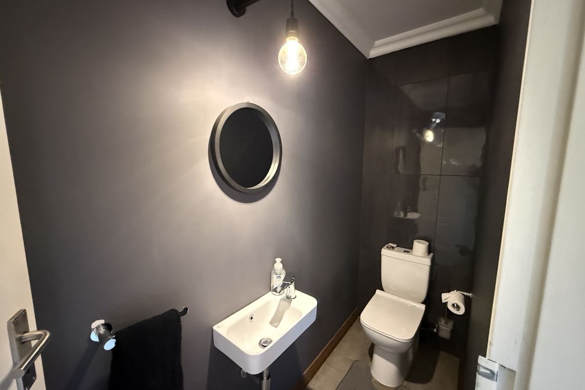 A modern guest bathroom featuring dark wall finishes, a wall-mounted basin, and a clean, contemporary toilet.