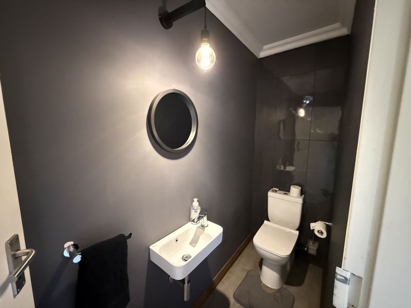 A modern guest bathroom featuring dark wall finishes, a wall-mounted basin, and a clean, contemporary toilet.