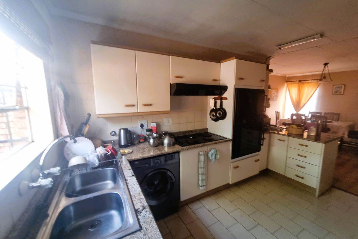 A functional kitchen featuring granite countertops, built-in oven, hob, and extractor fan, with tiled flooring and ample cabinetry, showing signs of wear and ceiling staining.