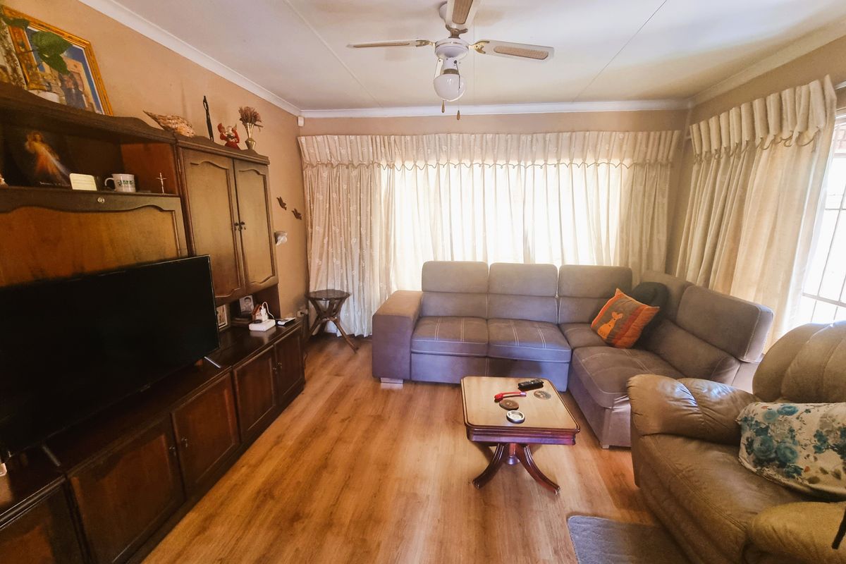 A comfortable living room featuring laminate flooring, a ceiling fan, and large windows dressed with floor-to-ceiling curtains.