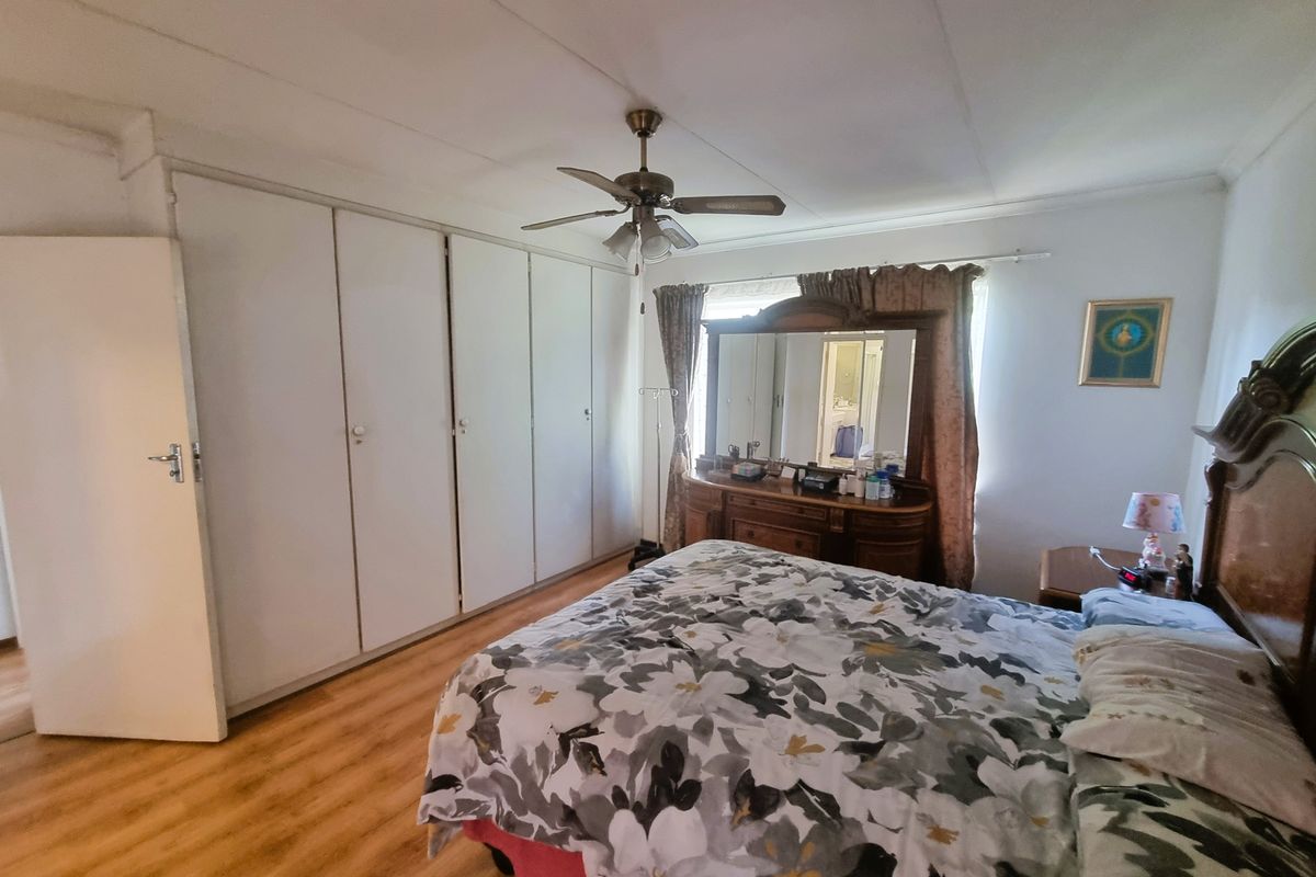 A spacious bedroom featuring light-toned laminate flooring, extensive built-in cupboards, and a central ceiling fan, offering a functional and well-lit living space.