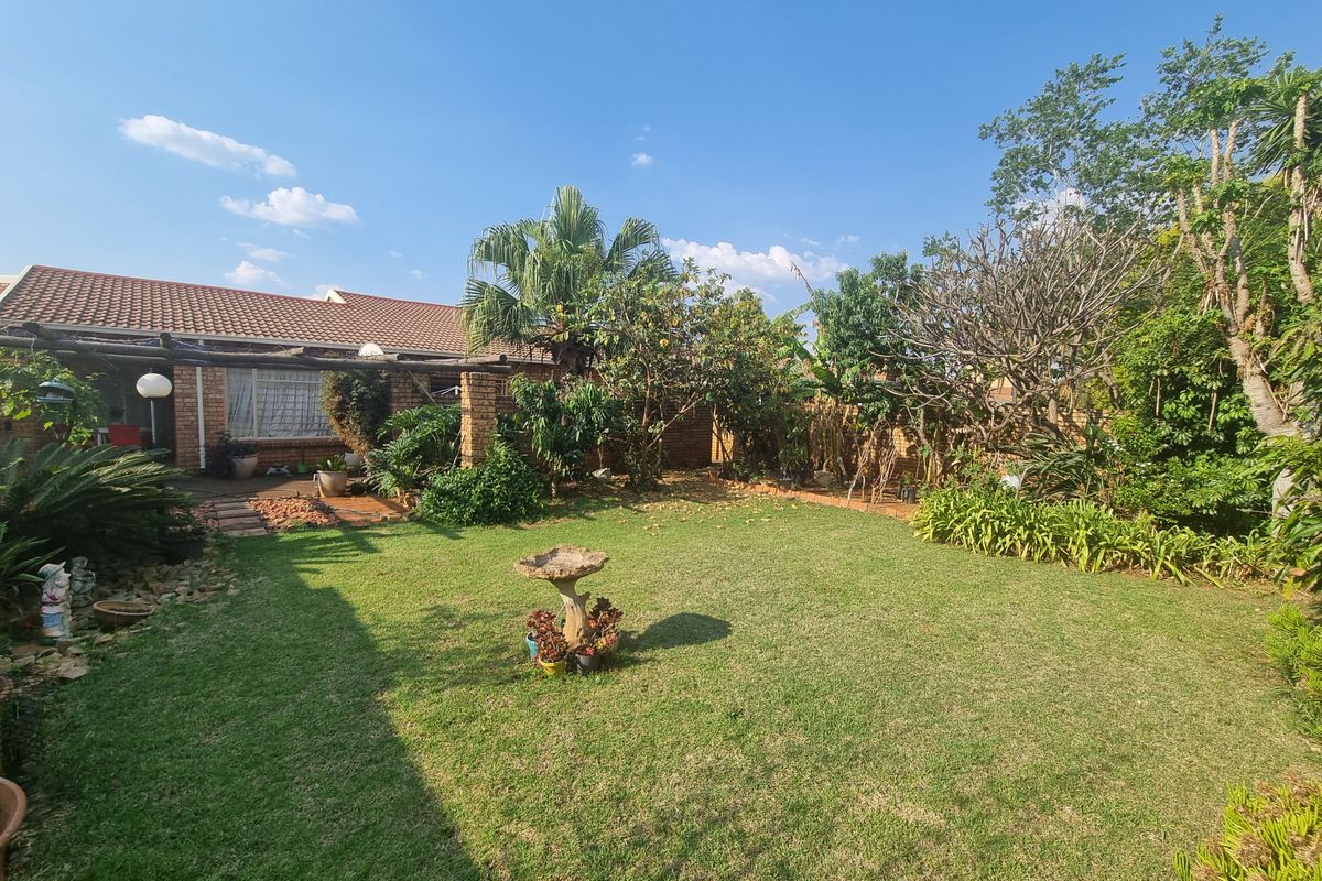 A private rear garden featuring a well-maintained lawn, established landscaping, and a covered pergola attached to the brick townhouse structure.