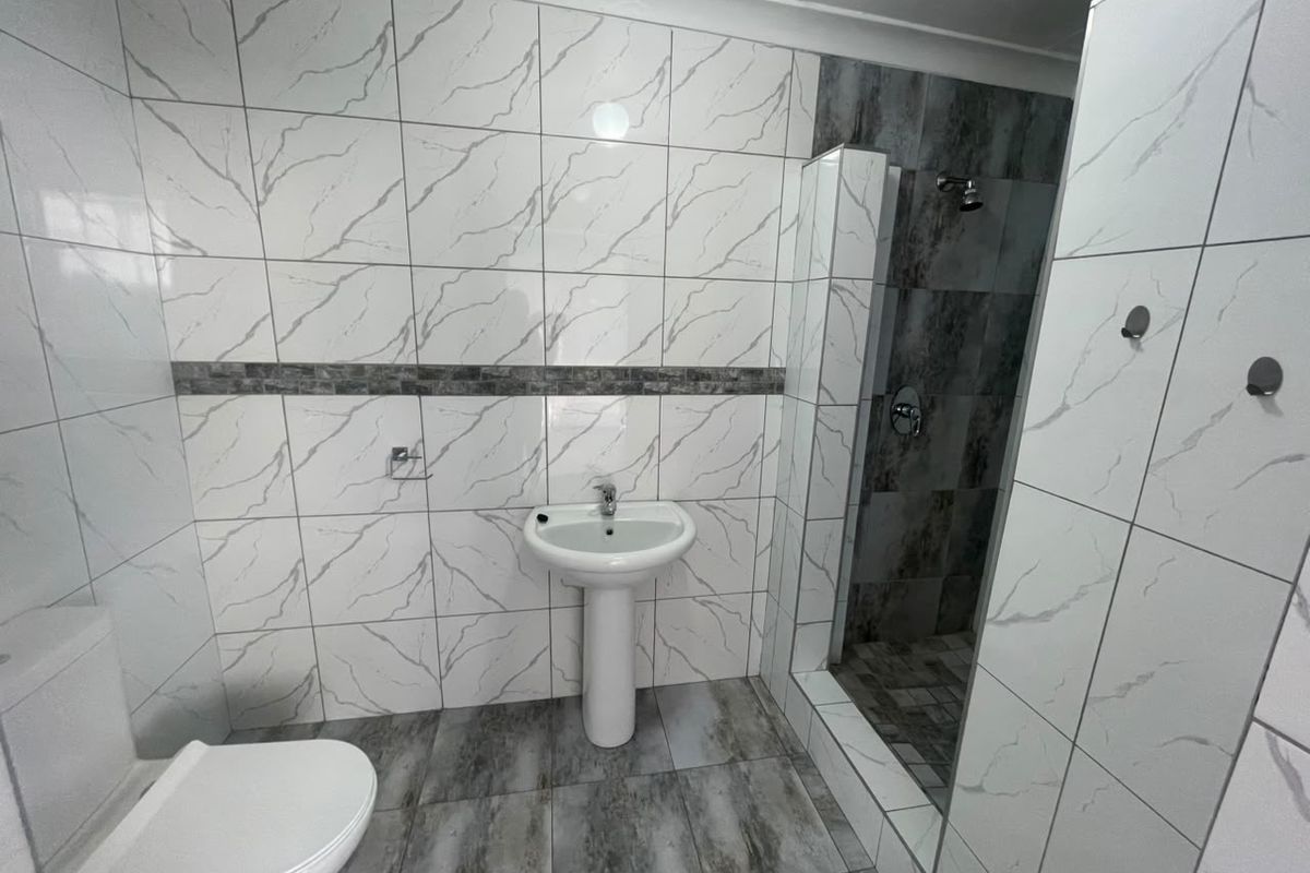 Modern bathroom featuring a pedestal basin, toilet, and a walk-in shower with contemporary marble-effect wall tiles and grey floor tiles.