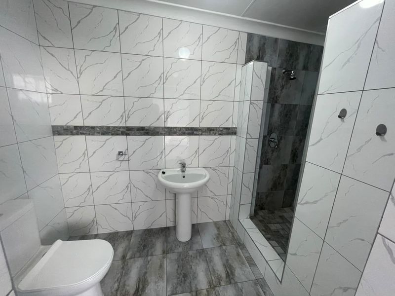 Modern bathroom featuring a pedestal basin, toilet, and a walk-in shower with contemporary marble-effect wall tiles and grey floor tiles.