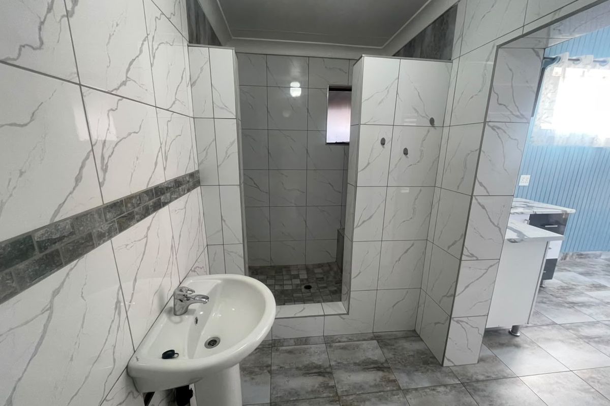 Modern bathroom featuring marble-effect wall tiling, a pedestal basin with chrome mixer tap, and a spacious walk-in shower area.