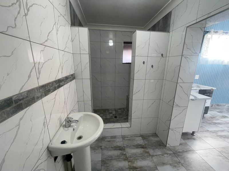 Modern bathroom featuring marble-effect wall tiling, a pedestal basin with chrome mixer tap, and a spacious walk-in shower area.