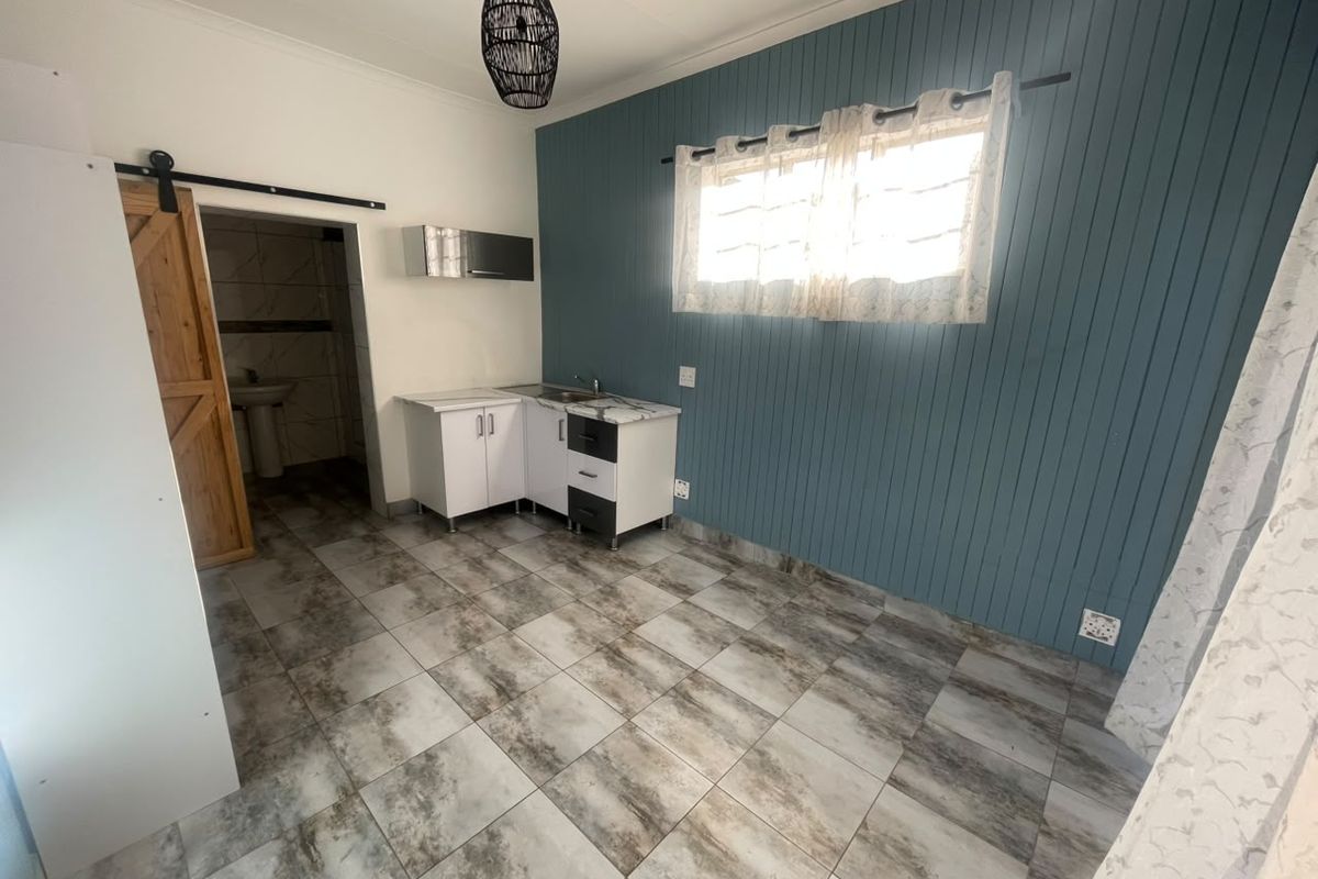 A compact kitchen area featuring tiled flooring, blue tongue and groove wall paneling, and a sliding barn door leading to an adjacent bathroom.