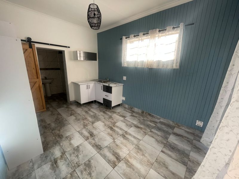 A compact kitchen area featuring tiled flooring, blue tongue and groove wall paneling, and a sliding barn door leading to an adjacent bathroom.