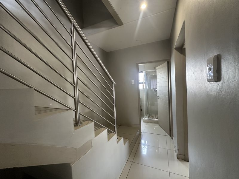 A bright hallway featuring tiled flooring and a modern stainless steel staircase railing, leading towards an adjacent bathroom area.