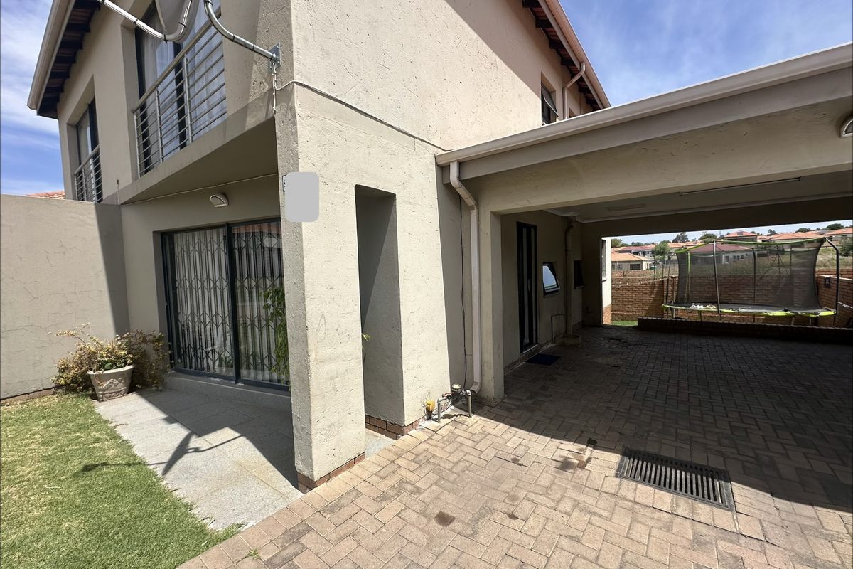 Rear exterior view of the property featuring a paved driveway, covered carport, and a sliding door leading to the living area.