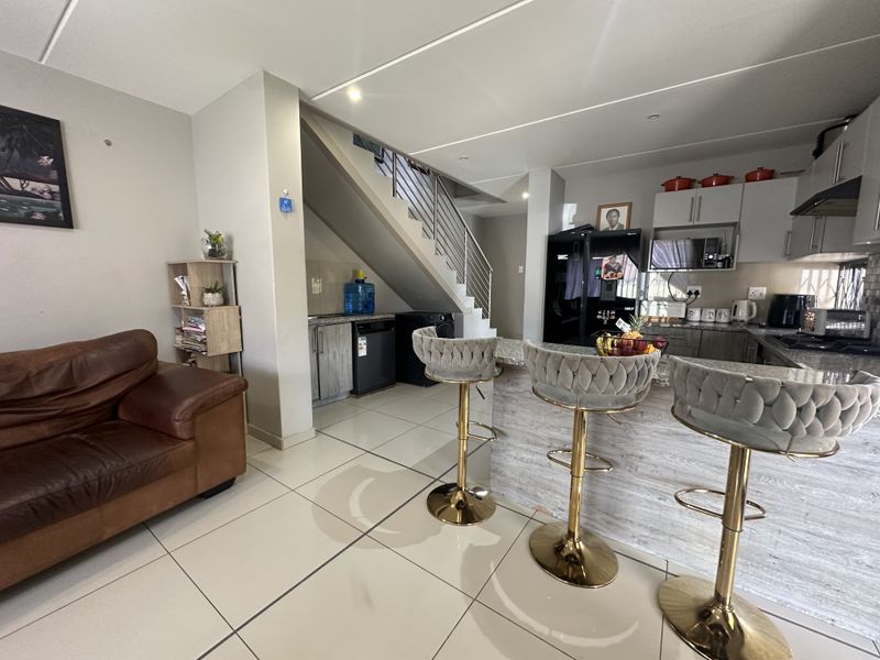 Open plan living and kitchen area featuring tiled floors, modern cabinetry, granite countertops, and a staircase with a contemporary metal balustrade.