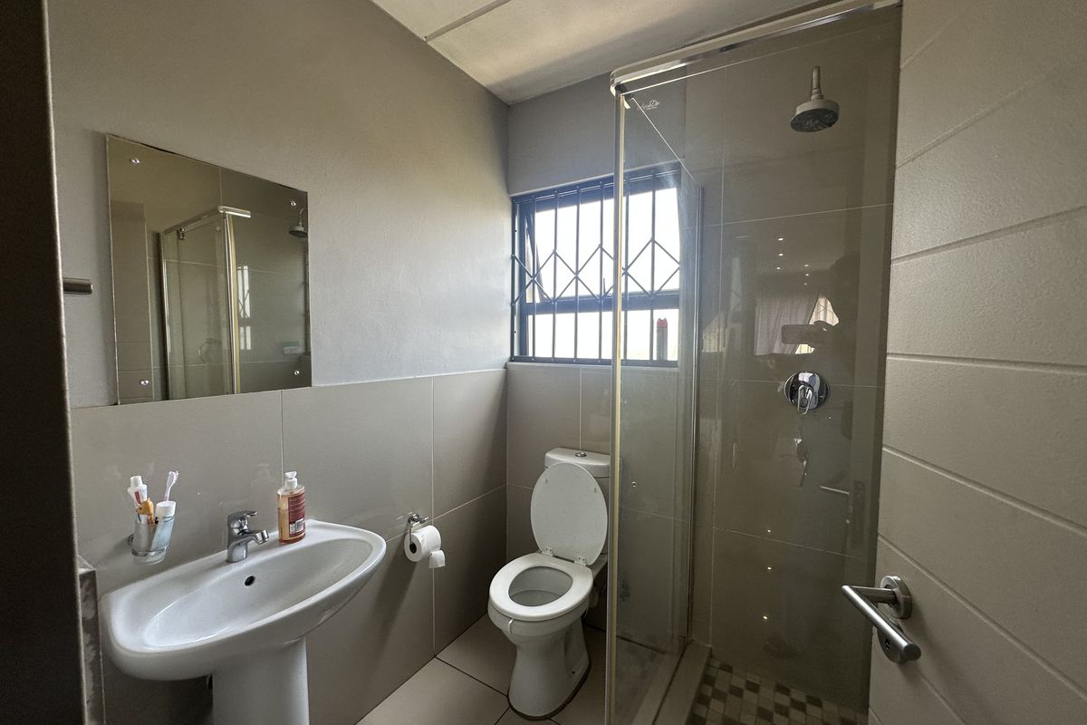 A functional bathroom featuring a pedestal basin, toilet, and a glass-enclosed shower with tiled finishes and security bars on the window.