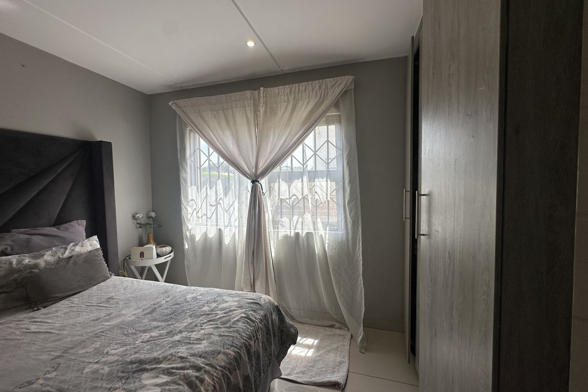 A well-maintained bedroom featuring neutral grey walls, tiled flooring, recessed ceiling lighting, and a built-in wardrobe with modern wood-grain finish.