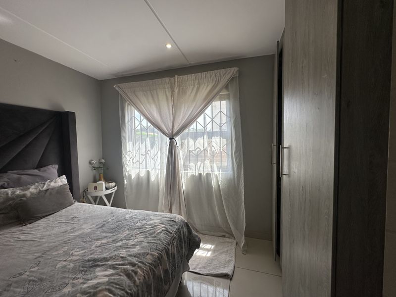 A well-maintained bedroom featuring neutral grey walls, tiled flooring, recessed ceiling lighting, and a built-in wardrobe with modern wood-grain finish.