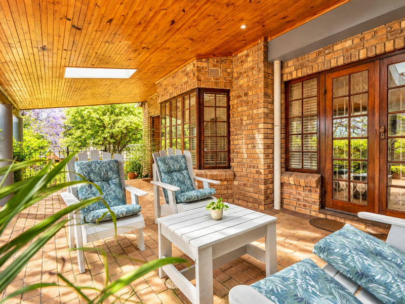 A covered patio featuring a warm timber-clad ceiling with a skylight, exposed brick walls, and classic timber-framed glass doors leading into the home.