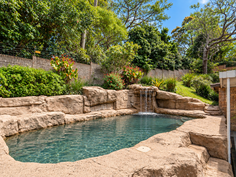 A landscaped rock-feature swimming pool with a built-in waterfall, set against a private garden with brick boundary walls and established trees.