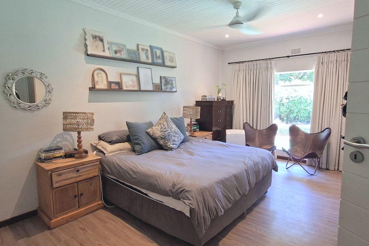 A well-maintained bedroom featuring laminate flooring, a tongue and groove ceiling with a fan, and direct access to the garden through a sliding door.