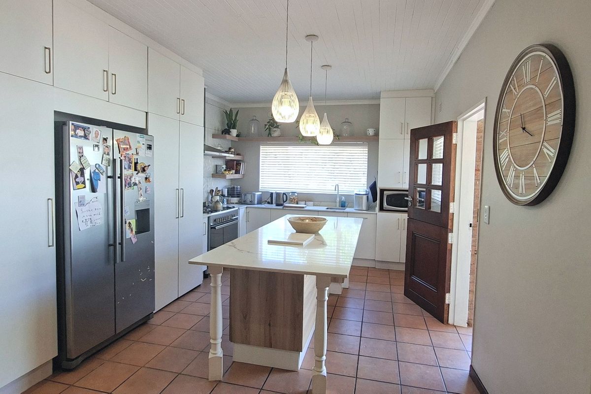 A well-appointed kitchen featuring extensive built-in cabinetry, a central island with stone countertop, stainless steel appliances, and durable tiled flooring.