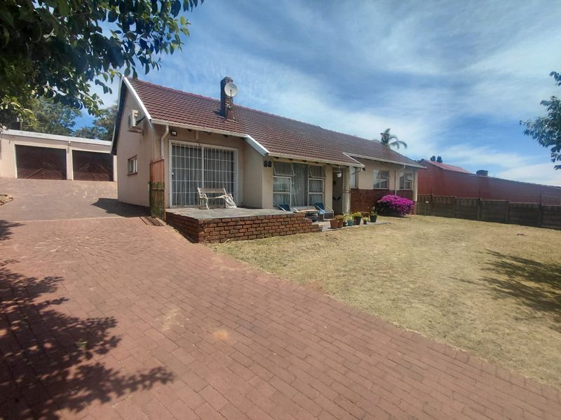 Front view of a single-story house featuring a tiled roof, brick driveway, attached double garage, and a paved patio area.