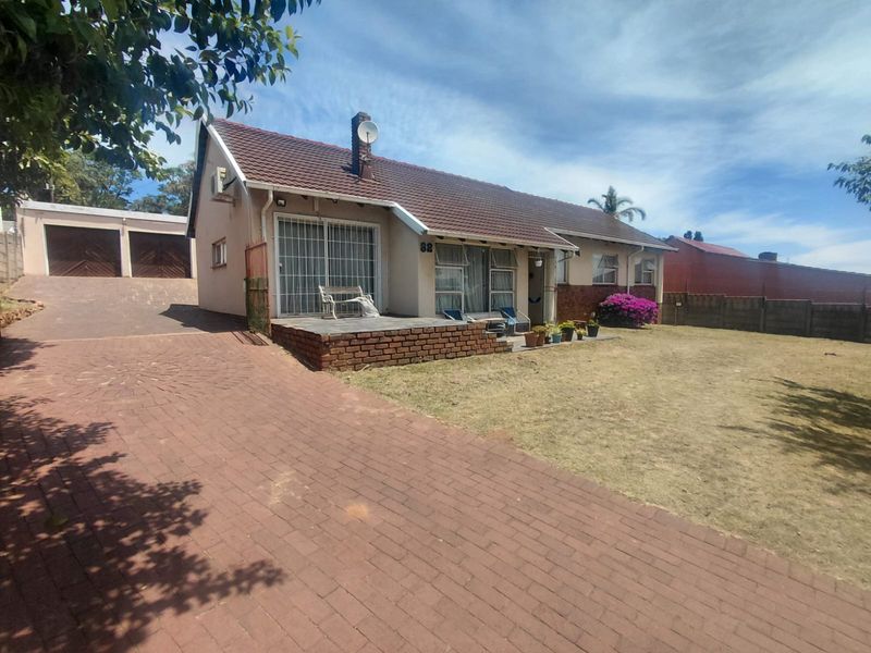 Front view of a single-story house featuring a tiled roof, brick driveway, attached double garage, and a small front patio area.