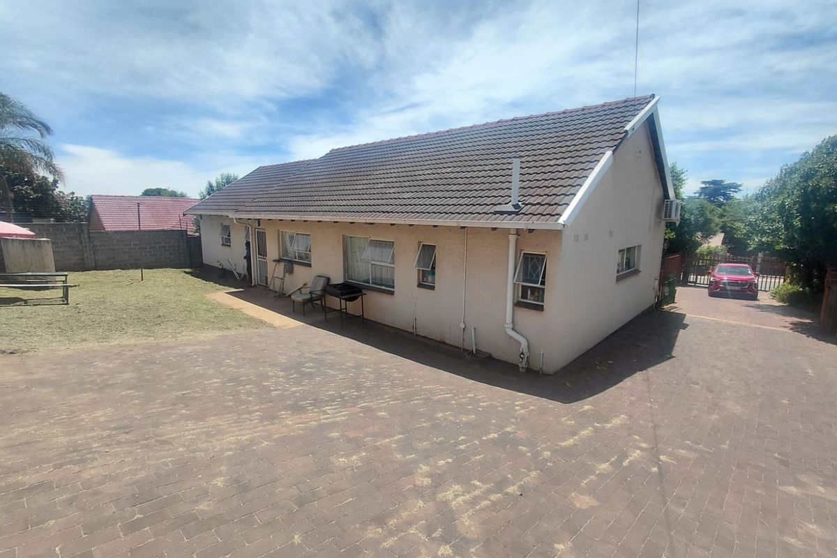 Rear view of the property featuring a tiled roof, paved driveway, and surrounding boundary wall with an installed air conditioning unit.