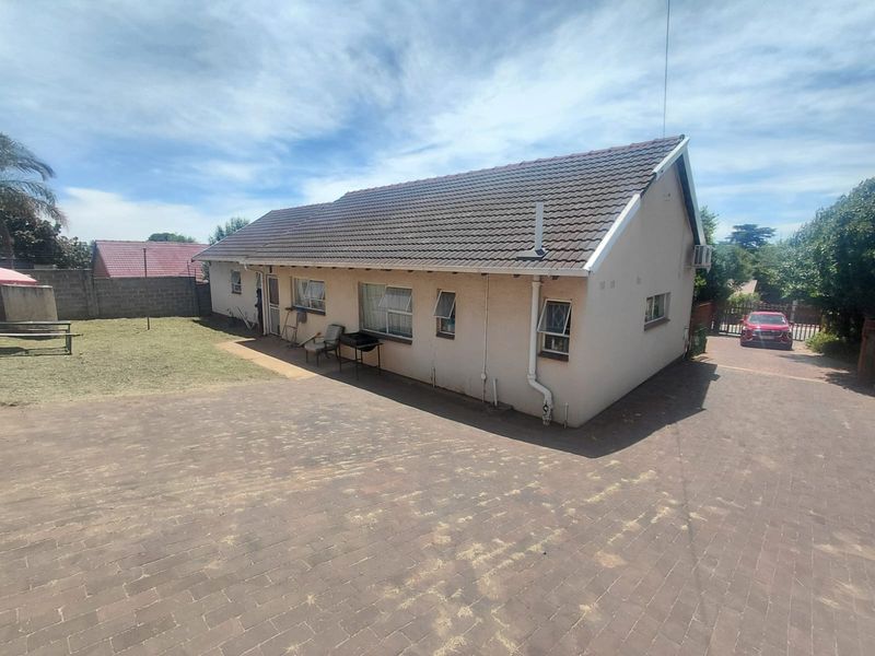 Rear view of the property featuring a tiled roof, paved driveway, and surrounding boundary wall with an installed air conditioning unit.