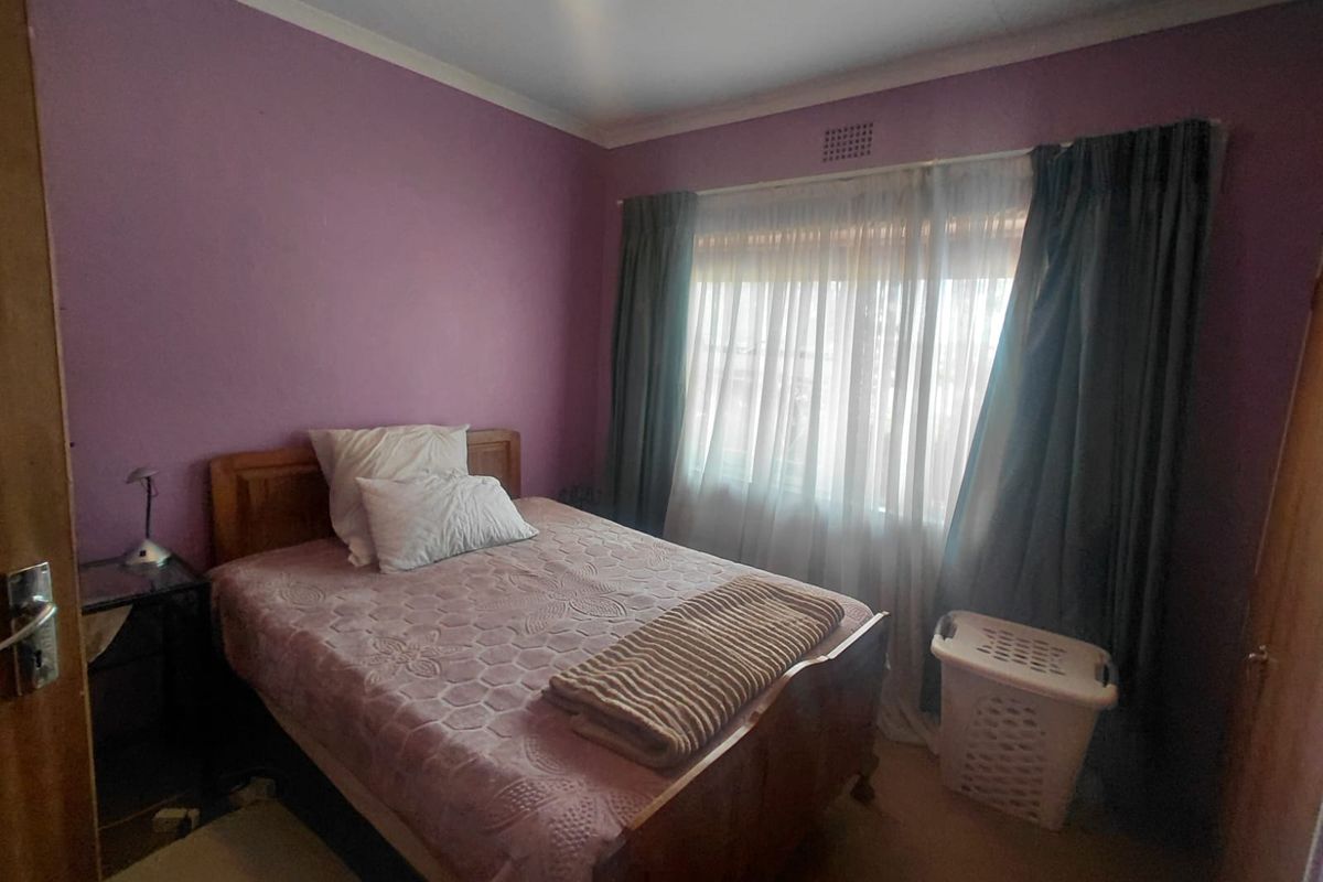 A standard bedroom featuring purple painted walls, a window with curtains, and a ventilation grille.