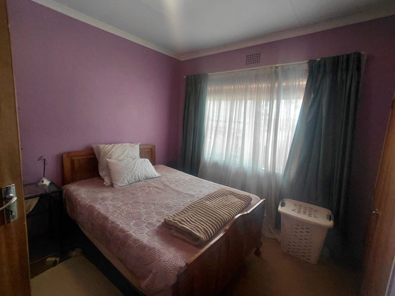 A standard bedroom featuring purple painted walls, a window with curtains, and a ventilation grille.