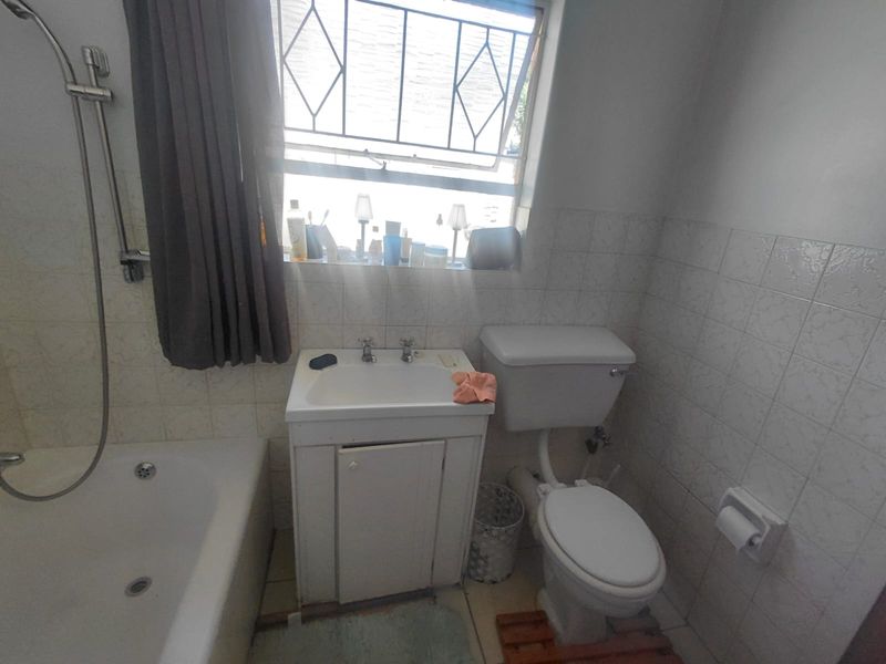 A functional bathroom featuring a bathtub with shower mixer, vanity basin, and toilet, finished with tiled walls and security bars on the window.
