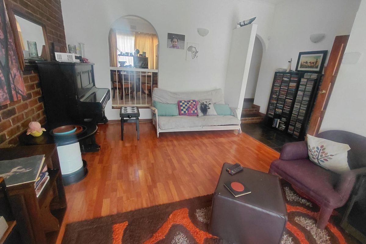 A living room featuring exposed brick fireplace detailing, timber flooring, and an arched doorway leading to an adjacent space.