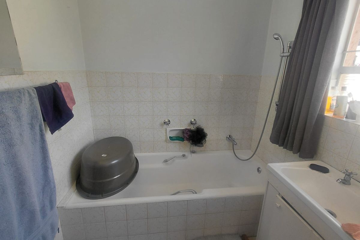 A functional bathroom featuring a built-in bathtub with a shower attachment and a vanity basin with tiled wall finishes.
