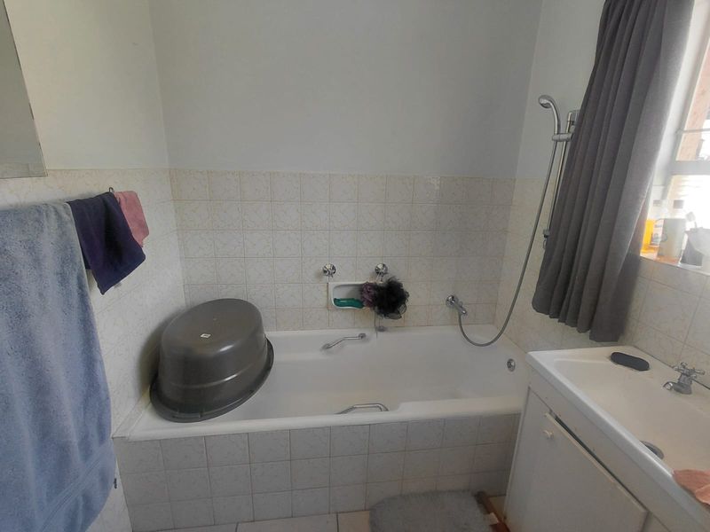 A functional bathroom featuring a built-in bathtub with a shower attachment and a vanity basin with tiled wall finishes.