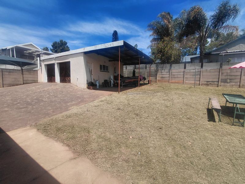 Rear view of the property featuring a double garage, a covered patio area, and a spacious backyard enclosed by precast concrete boundary walls.
