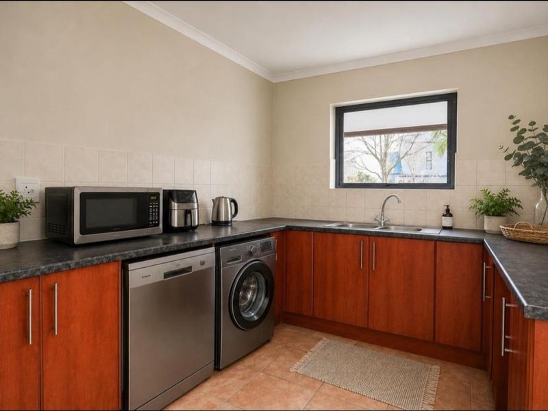 A functional kitchen featuring wood-finish cabinetry, dark laminate countertops, a double stainless steel sink, and tiled flooring with a neutral backsplash.