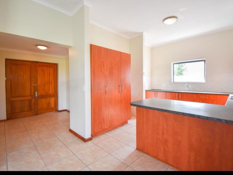Open plan kitchen area featuring wooden cabinetry, laminate countertops, and tiled flooring, adjacent to a spacious entrance hall with double wooden doors.