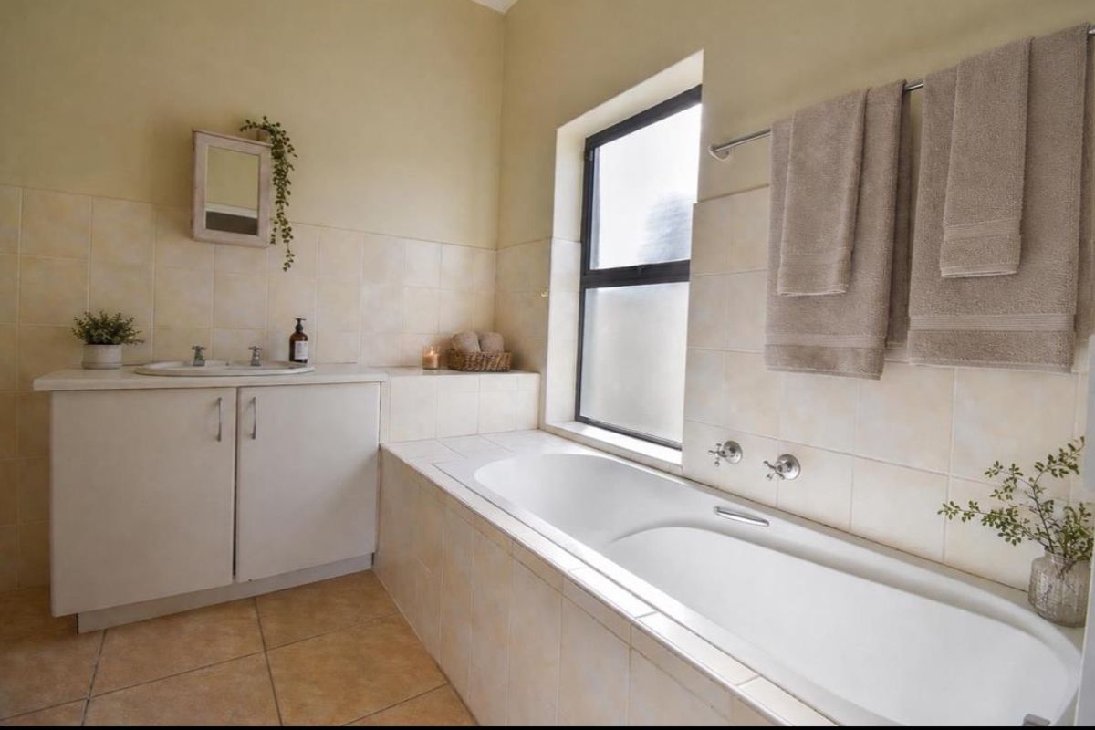 A functional bathroom featuring a built-in bathtub, tiled wall and floor finishes, a vanity cabinet with a basin, and a frosted window for privacy.