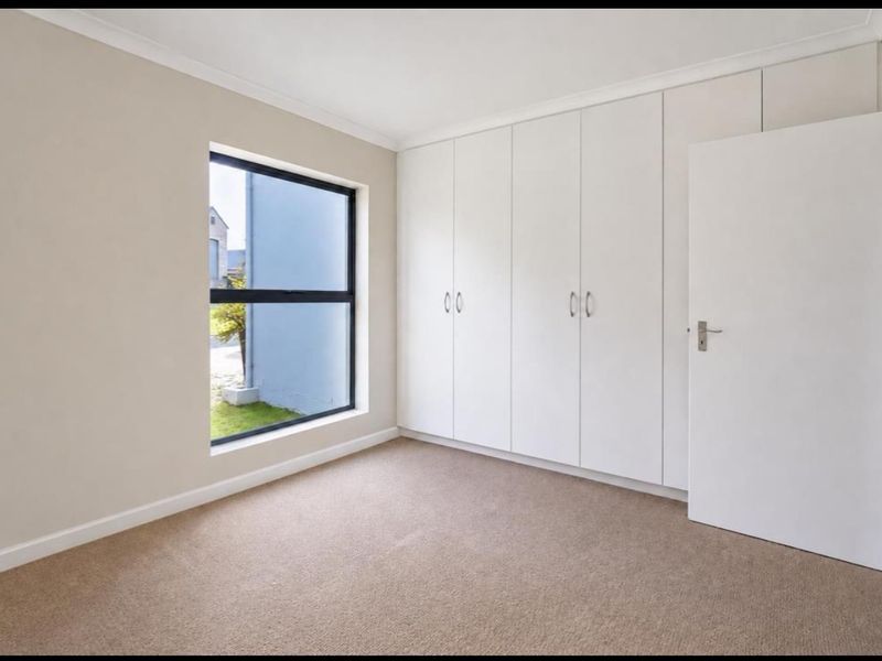 A clean, empty bedroom featuring neutral walls, carpeted flooring, and a wall of built-in cupboards with ample storage space.