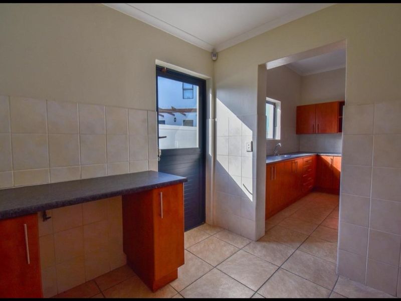 A functional scullery area featuring built-in wooden cabinetry, laminate countertops, tiled flooring, and direct access to the exterior.